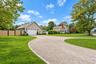 Expansive gravel driveway featuring stone paver curbing, mature landscaping, and a detached two-car garage