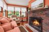 Red brick fireplace with a wood mantel, wood-finish flooring, and multiple windows with wood frames