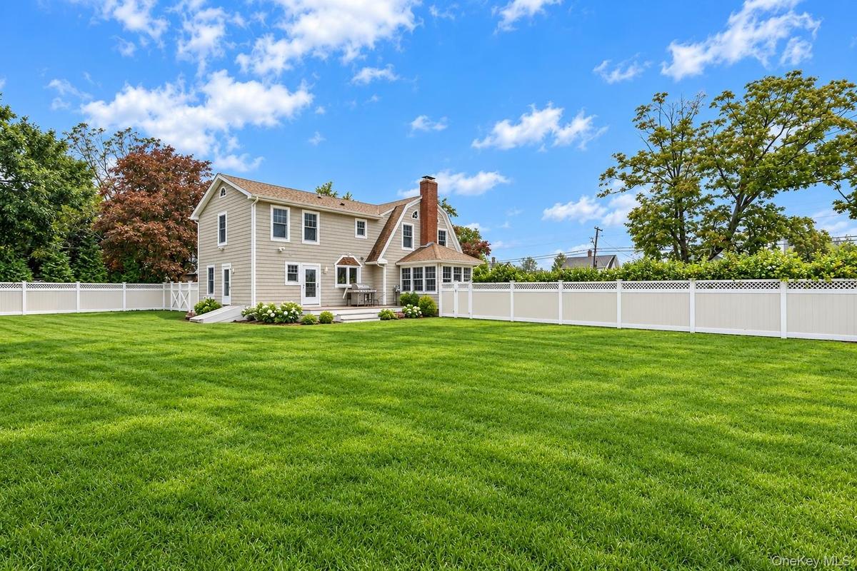 Expansive rear yard featuring a manicured lawn, full-perimeter privacy fencing, a multi-section gable roofline, and an exterior brick chimney