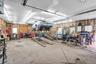 Workshop space featuring a concrete floor, built-in hydraulic vehicle lift, exposed stud wall framing, overhead fluorescent lighting, and two exterior