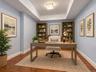 Virtually staged to showcase its potential as a stylish home office, this versatile space features distinctive tray ceiling detailing and warm wood fl