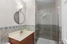 Wood-finish vanity with a molded countertop, glass-enclosed shower featuring a rainfall showerhead, and decorative tiled walls