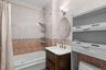 Full-wall tile surround, jetted soaking tub, dark wood-finish vanity with integrated sink, wall-mounted oval mirror, and fixed overhead cabinetry