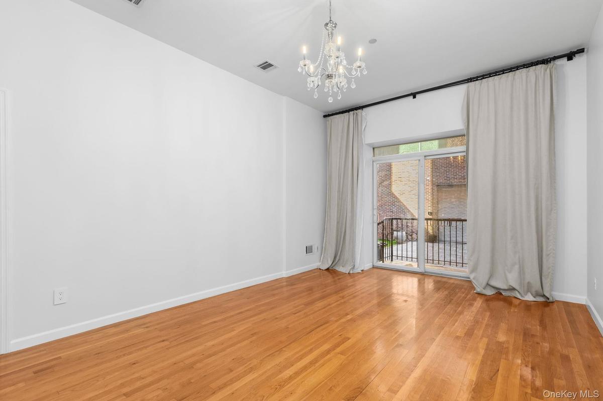 High-ceilinged room featuring wood-finish flooring, a multi-light crystal chandelier, and a sliding glass door to private patio with a decorative blac