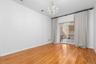 High-ceilinged room featuring wood-finish flooring, a multi-light crystal chandelier, and a sliding glass door to private patio with a decorative blac