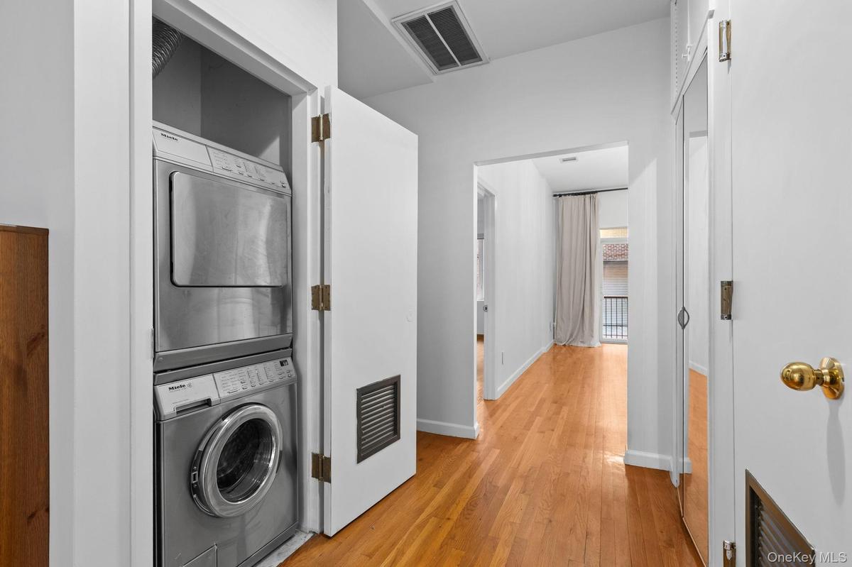 Stacked laundry unit with stainless steel appliances, wood-finish flooring, and mirrored closet doors