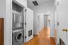 Stacked laundry unit with stainless steel appliances, wood-finish flooring, and mirrored closet doors