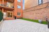 Private outdoor space featuring gray paver hardscaping, a synthetic turf lawn, red brick building exterior, and an elevated metal-railed balcony.
