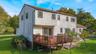 Two-story home with shingle siding, elevated wood deck, sliding glass door access, stone patio, and expansive lawn