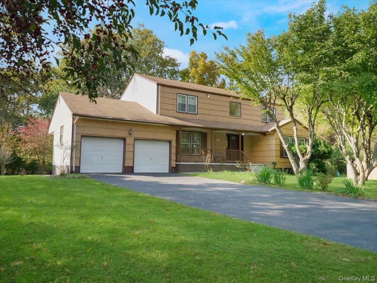 Two-story exterior featuring tan horizontal siding, a covered front porch with railing, an attached two-car garage, and an asphalt driveway situated o