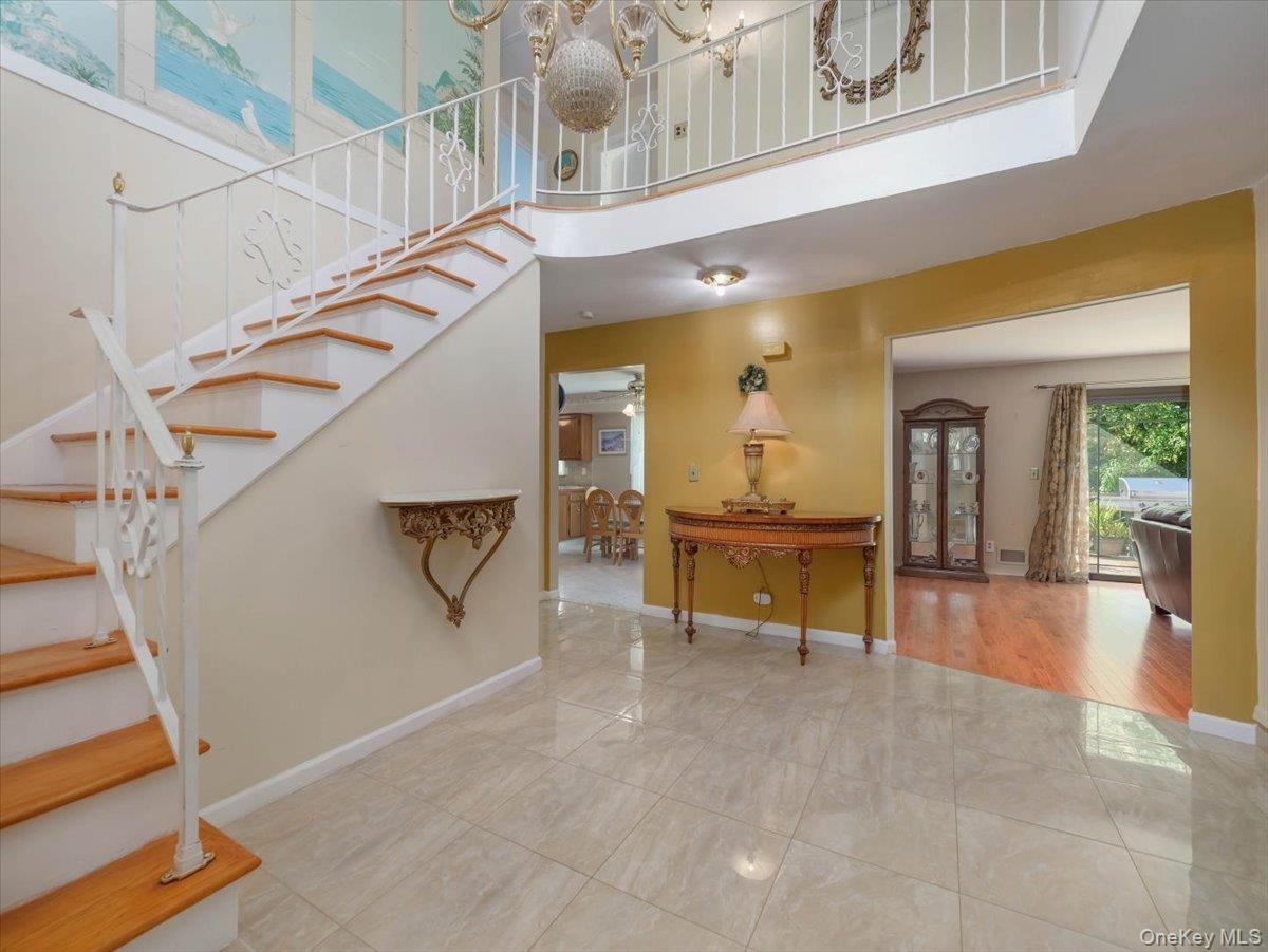 Foyer featuring large-format tile flooring, a curved staircase with white metal railings, wood-finish stair treads, and a crystal-style chandelier