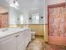 Dual-sink vanity with white cabinetry, oversized wall-mounted mirror, mosaic tile backsplash, and stone-finish flooring