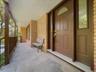 Covered front porch featuring a brick exterior, solid wood-finish entry door with leaded glass inserts, and wood railing