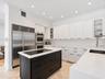 Kitchen featuring white shaker-style cabinetry, contrasting black center island, built-in stainless steel double wall oven, integrated refrigerator, a