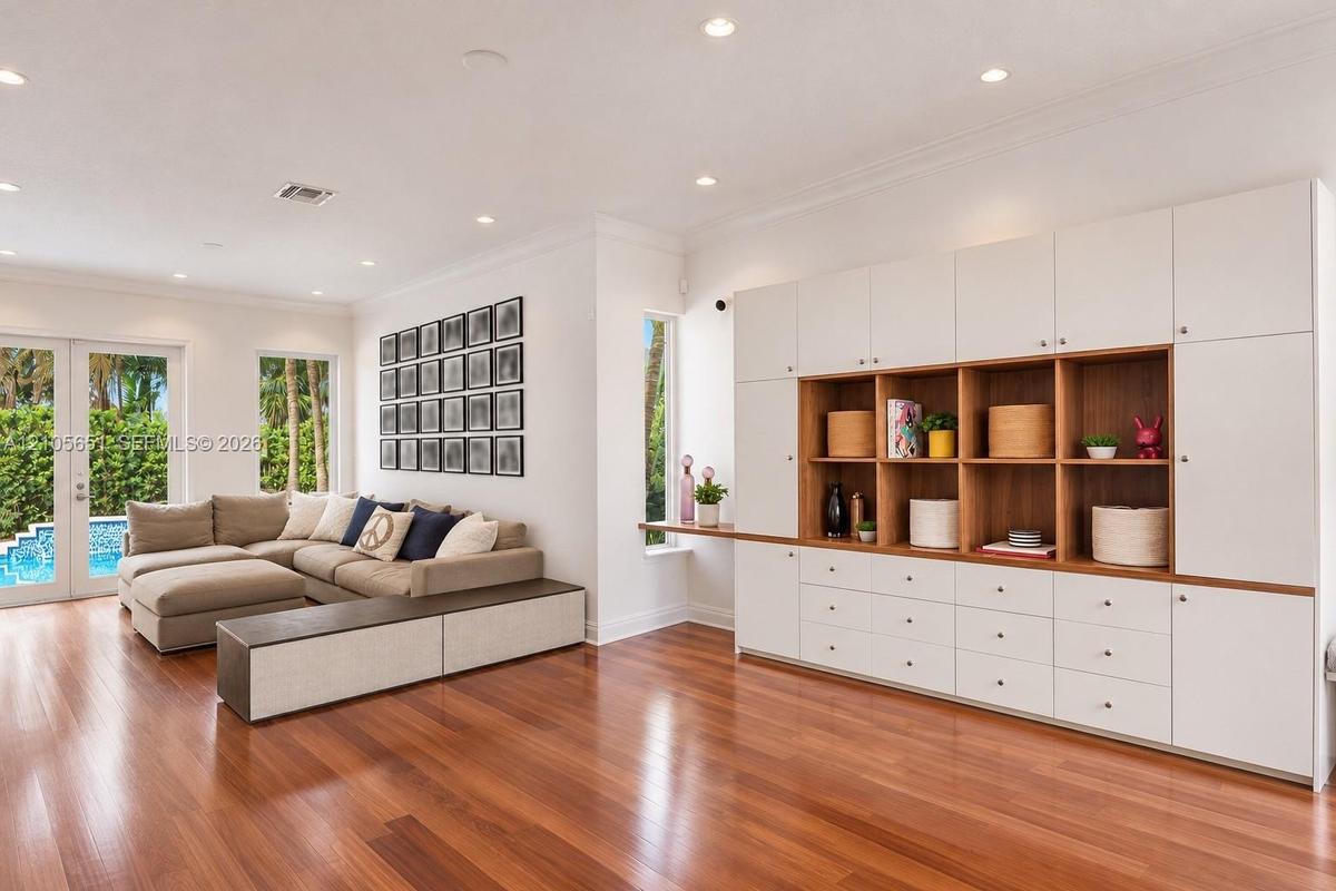 Living area featuring wood-finish flooring, extensive built-in cabinetry with integrated shelving and drawers, crown molding, and recessed lighting