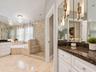 Bathroom featuring stone-finish flooring and wall tiling, dual white vanities with dark stone countertops, a frameless glass-enclosed shower with a bu