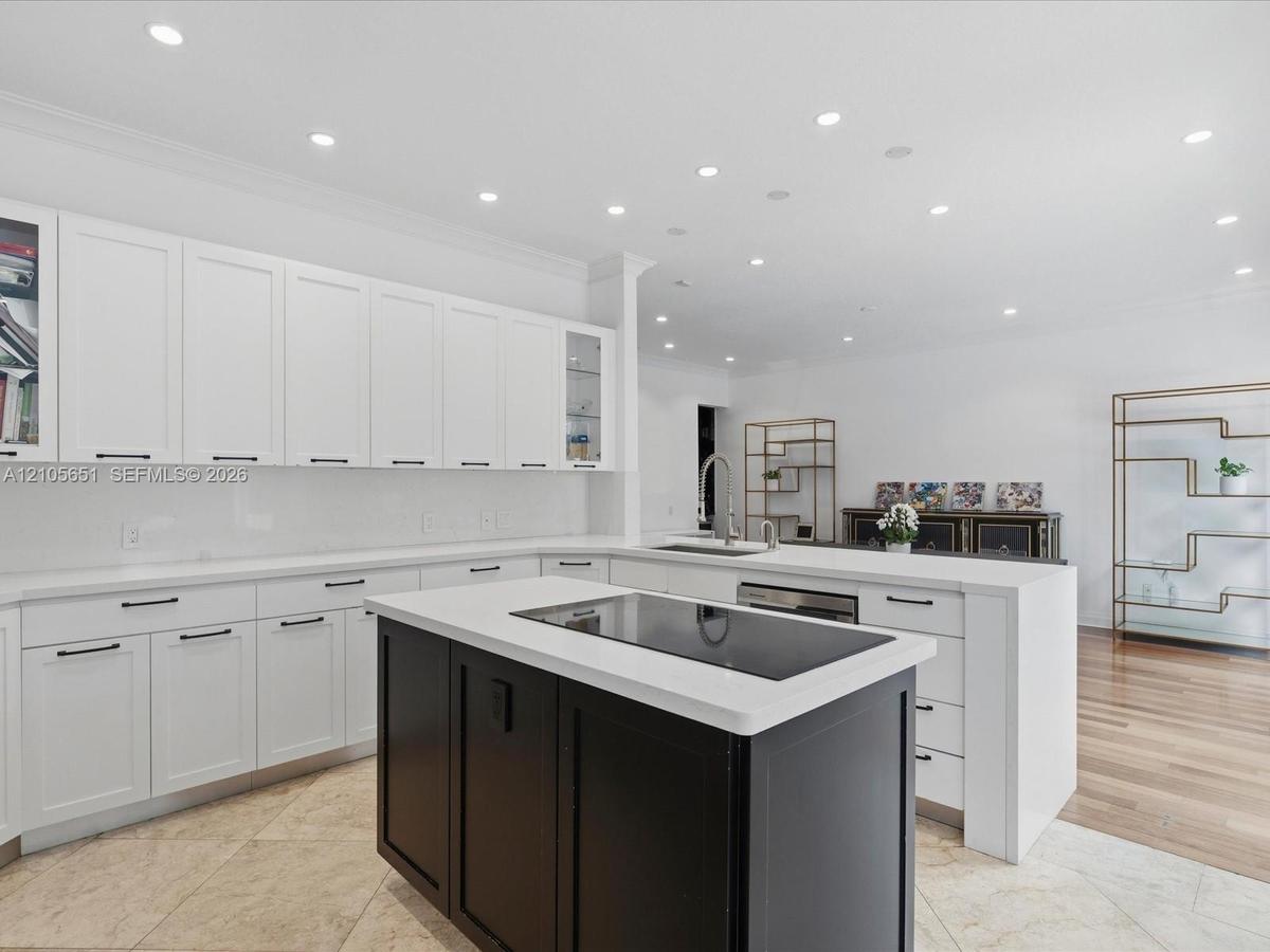 Kitchen featuring white cabinetry with glass-front display panels, central island with a contrasting dark finish, integrated stovetop, recessed lighti