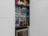 Built-in recessed display cabinet featuring mirrored backing, glass shelving, a dark stone countertop, and an integrated stainless steel wine refriger