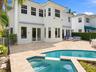 Two-story stucco exterior featuring a stone-paved patio, custom swimming pool with integrated spa, multi-pane windows, and French door entryways