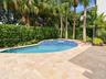 Outdoor area featuring a stone-paver patio, a swimming pool with blue tile accents, a raised spillway, and mature perimeter landscaping