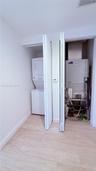 Utility closet featuring a stacked washer and dryer unit, HVAC equipment, and light-toned wood-finish flooring