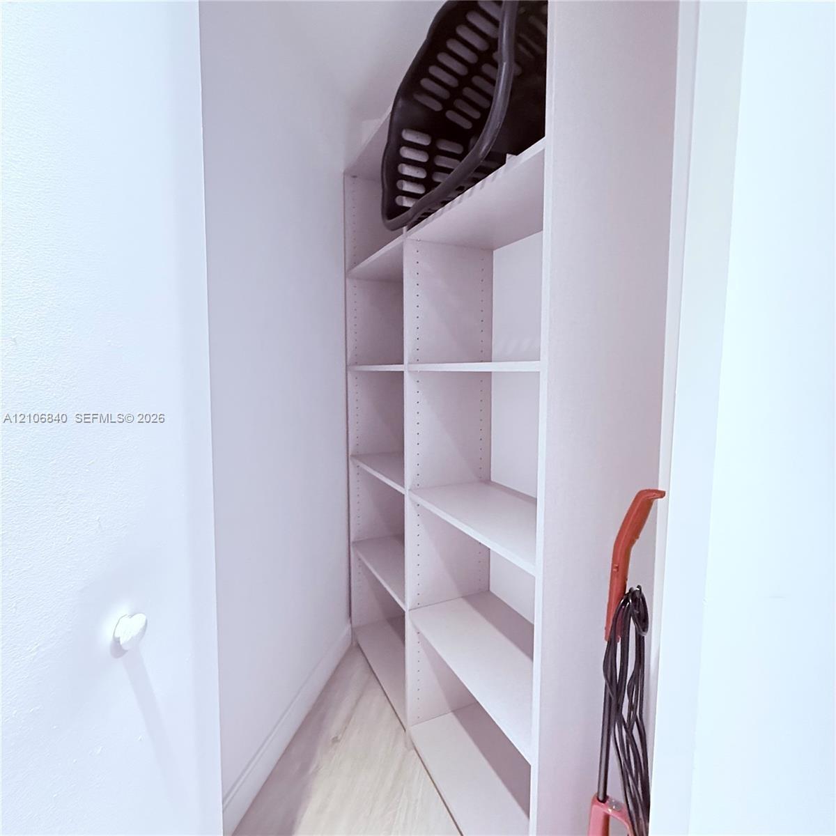 Built-in, floor-to-ceiling white shelving with adjustable cabinetry and light-toned wood-finish flooring