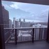 Covered balcony featuring concrete flooring and a dark metal railing with glass panel inserts, framed by a high-rise urban skyline