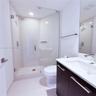 Walk-in shower with frameless glass enclosure, dark-finish cabinetry, solid-surface vanity countertop with integrated sink, polished chrome faucet, an