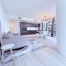 Open-concept living space featuring wood-finish flooring, dark cabinetry, stainless steel appliances, floor-to-ceiling glass, and a modern sculptural 