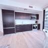 Kitchen featuring dark-finish cabinetry, light-toned stone-surface countertops, wood-finish flooring, and integrated stainless-steel appliances