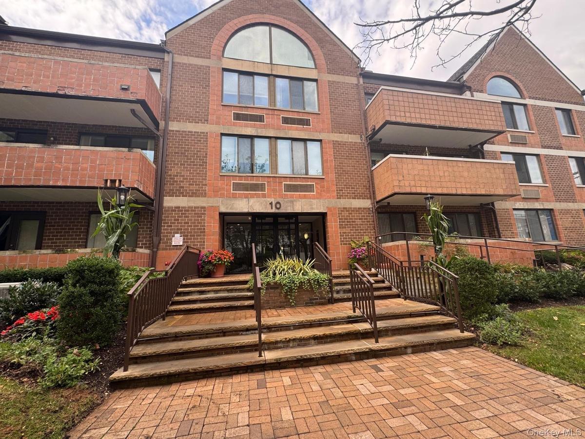 Multi-story brick exterior featuring arched windows, a paved walkway, and tiered stone entrance steps with metal railings