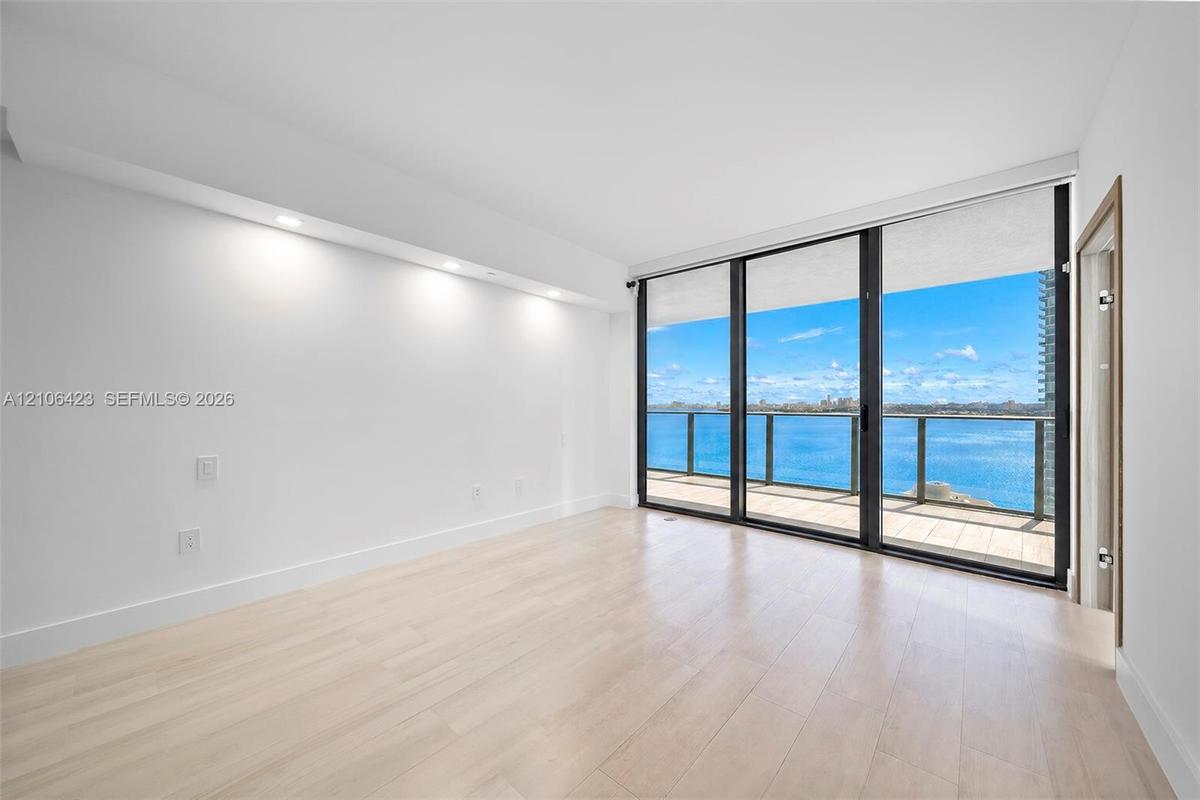 Floor-to-ceiling windows, wood-finish flooring, recessed ceiling lighting, and a private balcony featuring a water backdrop
