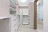 Walk-in closet featuring custom white cabinetry, open shelving, integrated drawer units, and tile flooring, including a glass-enclosed shower with woo
