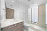 Bathroom featuring a floating wood-finish vanity with a white countertop, large frameless mirror, glass-enclosed walk-in shower with floor-to-ceiling 