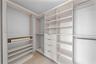 Custom walk-in closet featuring light-toned built-in cabinetry, floor-to-ceiling shelving, integrated hanging rods, and a multi-drawer dresser unit