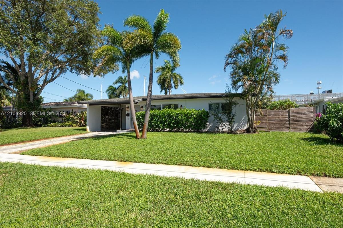 Single-story residence featuring a low-slope roof, light-toned exterior finish, decorative entry screen, mature palm trees, and manicured lawn