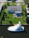 Waterfront property featuring a private dock, concrete patio, expansive lawn, and mature palm trees