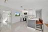 Kitchen featuring white cabinetry, stainless steel appliances, a central island with a grey paneled base, quartz countertops, and neutral tile floorin
