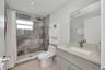 Full-height shower enclosure featuring stone-tiled walls and an overhead rain showerhead, complemented by a stone-topped vanity with an integrated bas