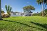 Expansive backyard featuring a sprawling grass lawn, mature trees, and a white exterior residence with a concrete patio