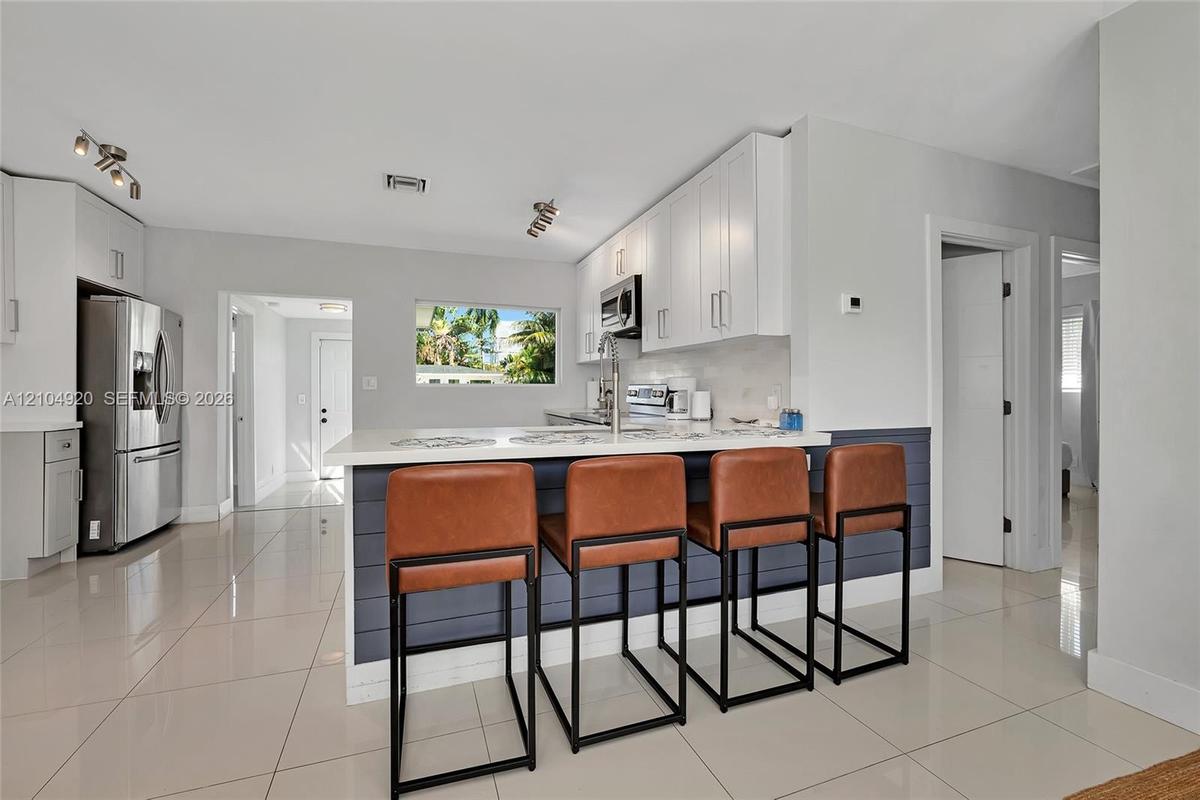 Kitchen featuring white cabinetry, quartz countertops, a shiplap-accented breakfast bar, polished tile flooring, and stainless steel appliances