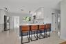 Kitchen featuring white cabinetry, quartz countertops, a shiplap-accented breakfast bar, polished tile flooring, and stainless steel appliances