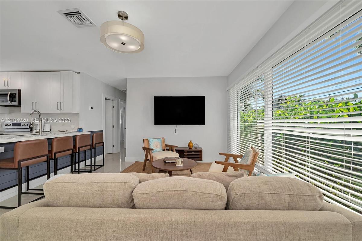Open-concept interior featuring large-format floor tiling, custom white cabinetry, a spacious kitchen island with stone surfacing, and expansive floor