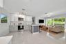 Kitchen featuring white shaker-style cabinetry, stainless steel appliances, a central island with a grey paneled base, quartz countertops, and large-f