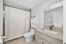 Bathroom featuring a stone-surface vanity with an integrated rectangular sink, wall-spanning mirror, one-piece toilet, and tile shower surround