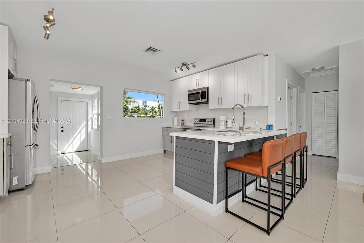 Kitchen featuring white cabinetry, an island with grey shiplap paneling, stainless steel appliances, and large-format tile flooring
