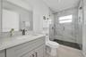 Bathroom featuring a grey vanity with a rectangular sink, stone-finish countertop, walk-in shower with floor-to-ceiling tile, and a wall-mounted glass