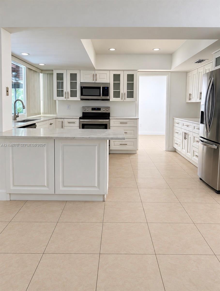 Kitchen featuring white shaker-style cabinetry, a peninsula with stone-finish countertops, stainless steel appliances, and tile flooring