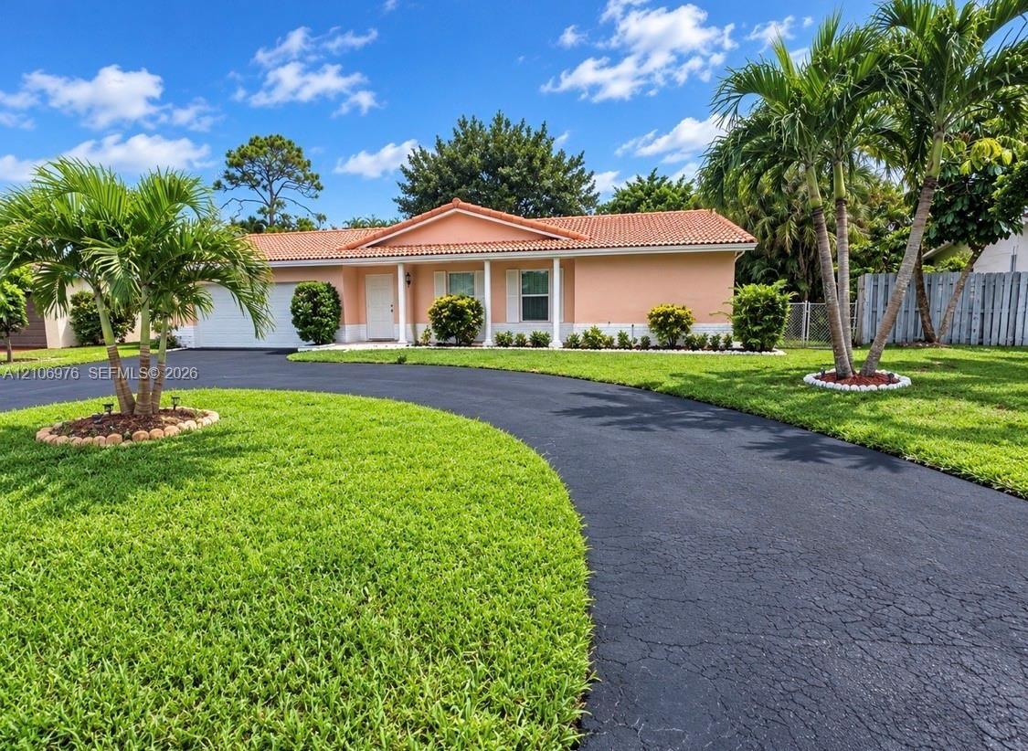Single-story residence featuring a tile roof, covered front entrance with structural columns, and an expansive paved circular driveway situated on a l
