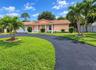 Single-story residence featuring a tile roof, covered front entrance with structural columns, and an expansive paved circular driveway situated on a l